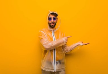 Yağmur ceketi giyen genç adam eliyle bir şeyler tutuyor.