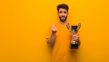 Elinde kupa tutan genç bir adam ihtiyaç jesti yapıyor.