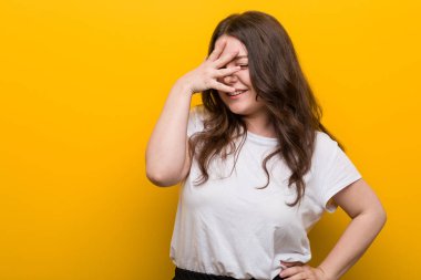 Genç, kıvrımlı, kilolu bir kadın kameraya parmaklarıyla göz kırpıyor, utanarak yüzünü kapatıyor..