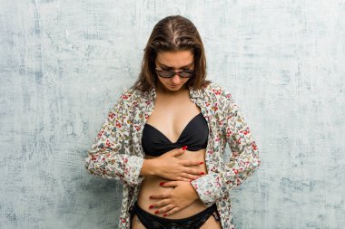Bikini giyen genç Avrupalı kadın, mide ağrısı, acı verici hastalık konsepti.