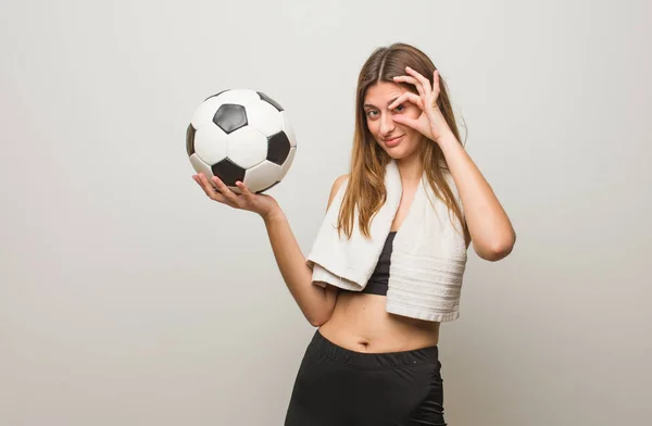 年轻的俄罗斯女子自信地对着眼睛做一个好的手势 拿着足球 — 图库照片