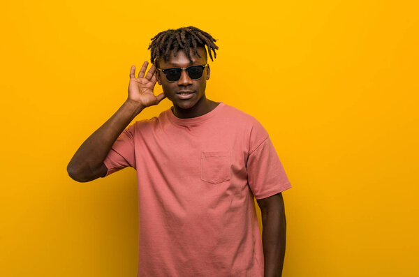 Young casual black man wearing sunglasses trying to listening a gossip.