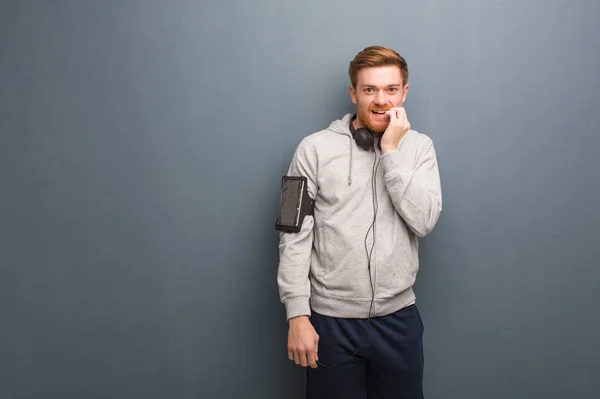 Young fitness redhead man biting nails, nervous and very anxious