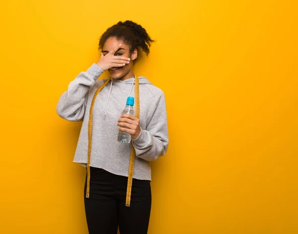 Young fitness black woman embarrassed and laughing at the same time.Holding a water bottle.