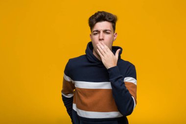 Kapüşonlu, esneyen, ağzı kapalı, yorgun bir jest yapan genç bir adam..