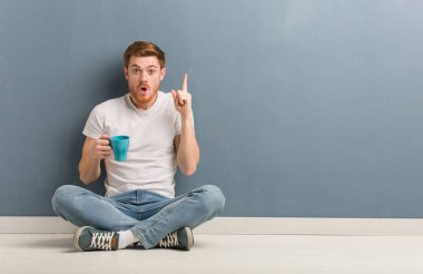 Genç kızıl saçlı öğrenci yerde oturuyor ve harika bir fikir üretiyor. Yaratıcılık kavramı. Elinde bir kahve fincanı var..