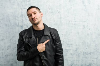 Genç rockçı adam gülümsüyor ve boş alanda bir şeyler gösteriyor..