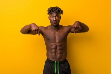 Genç siyahi adam mayo giyip parmaklarıyla aşağıya bakıyor, olumlu bir his..