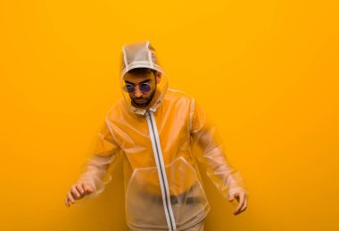 Yağmurluk giyen genç adam neşeli ve gülümsüyor.