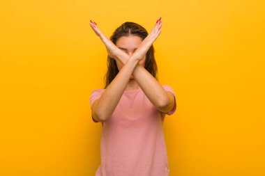 Genç Avrupalı kadın sarı arka plan iki silah çapraz tutmak üzerinde izole, inkar kavramı.