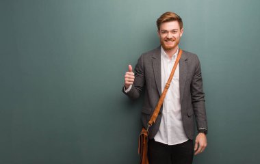 Genç kızıl saçlı iş adamı gülümsüyor ve başparmağını kaldırıyor.