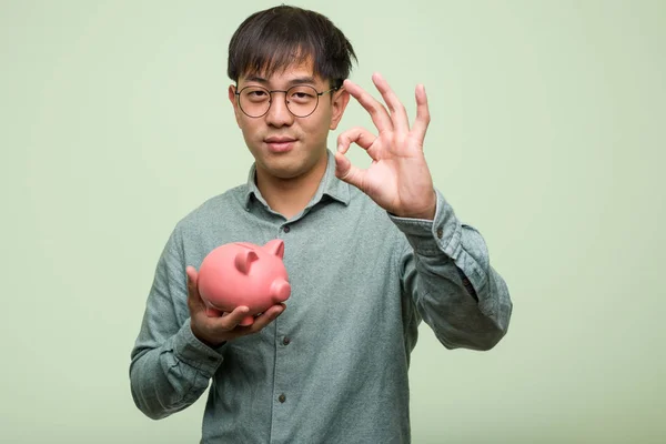 Junge Asiatische Mann Hält Ein Sparschwein Fröhlich Und Zuversichtlich Dabei — Stockfoto