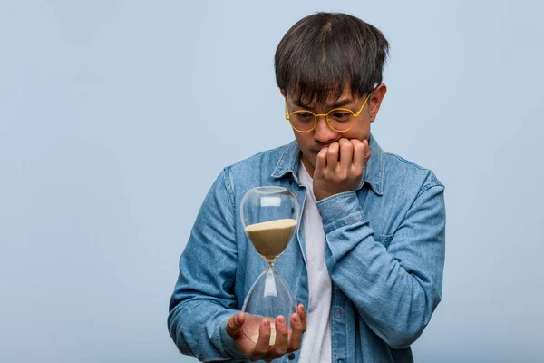Young Chinese Man Holding Sand Timer Biting Nails Nervous Very — Stock Photo, Image
