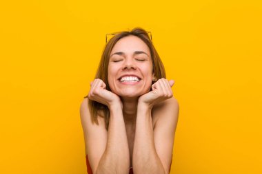 Bikini ve güneş gözlüğü takan genç beyaz kadın yumruğunu kaldırıyor, mutlu ve başarılı hissediyor. Zafer konsepti.