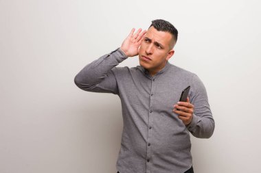 Young latin man holding a phone try to listening a gossip