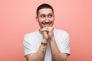 Genç adam ellerini çenesinin altında tutuyor, mutlu bir şekilde yan tarafa bakıyor..