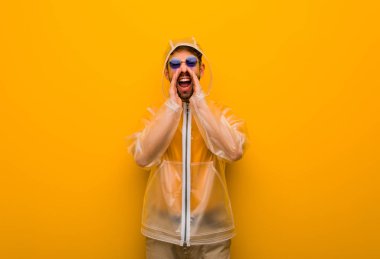 Yağmurluk giymiş genç bir adam cephede mutlu bir şeyler bağırıyor.