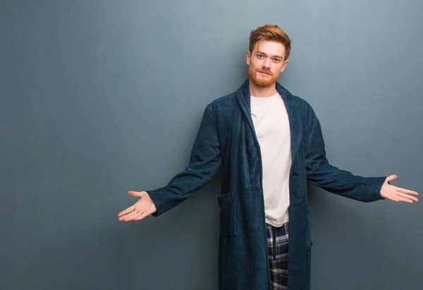 Young redhead man in pajama inviting to come