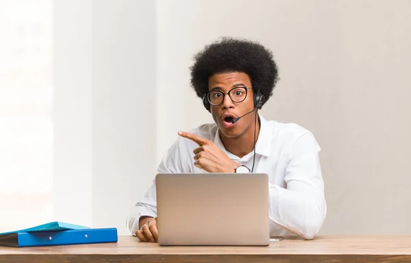 Young telemarketer black man pointing to the side