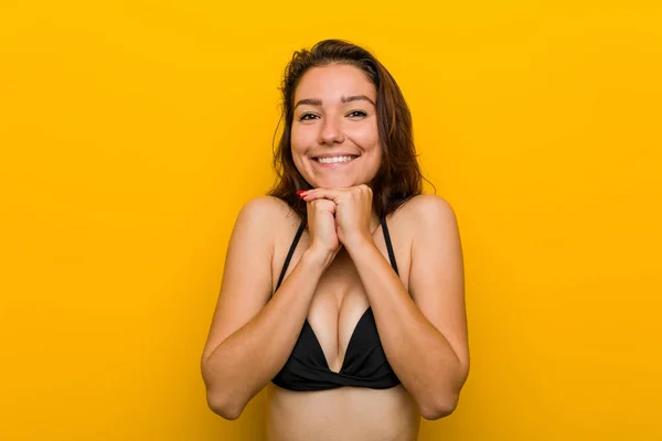 Young european woman wearing bikini keeps hands under chin, is looking happily aside.