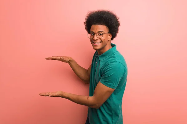 Jovem Afro Americano Sobre Uma Parede Rosa Segurando Algo Muito — Fotografia de Stock