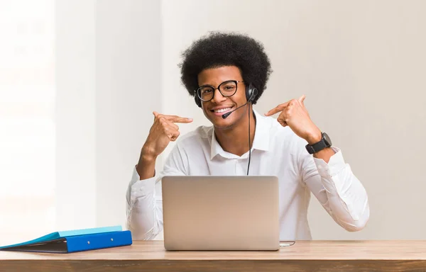 Young telemarketer black man smiles, pointing mouth