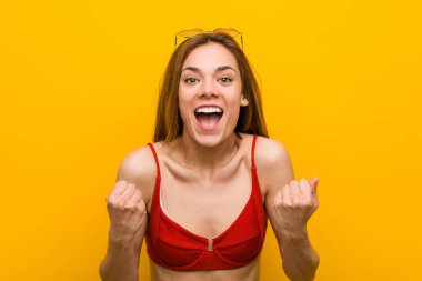 Young caucasian woman wearing bikini and sunglasses cheering carefree and excited. Victory concept.