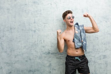 Genç, beyaz bir adam mayo giyiyor. Zafer kazandıktan sonra yumruğunu kaldırıyor..