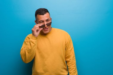 Young colombian man winking, funny, friendly and carefree gesture