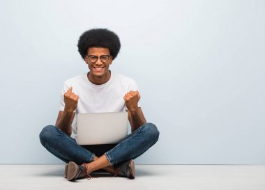 Genç siyah bir adam dizüstü bilgisayarla yerde oturuyor. Şaşırmış ve şok olmuş.