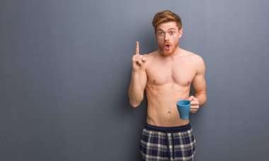 Genç, üstsüz, kızıl saçlı adamın harika bir fikri var. Yaratıcılık kavramı. Elinde bir kahve fincanı var..