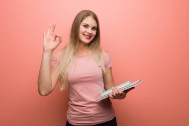 Genç, güzel Rus kız neşeli ve kendinden emin, iyi bir jest yapıyor. Elinde kitaplar var..