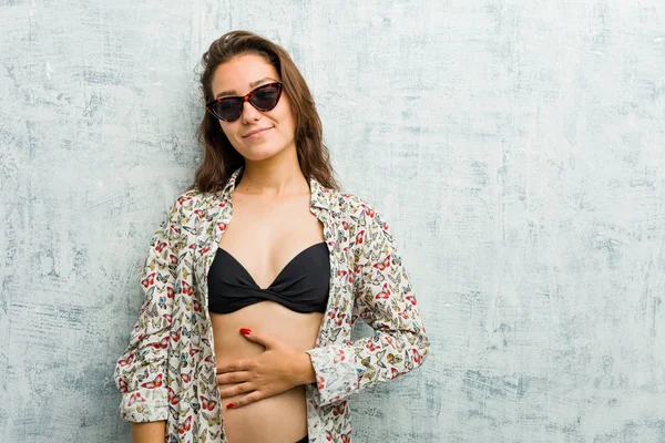 Bikini giyen genç Avrupalı kadın göbeğe dokunuyor, nazikçe gülümsüyor, yemek yiyor ve tatmin oluyor..