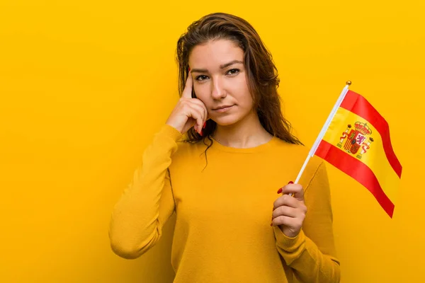 Молодая Европейская Женщина Испанским Флагом Указывая Пальцем Висок Думая Сосредоточилась — стоковое фото