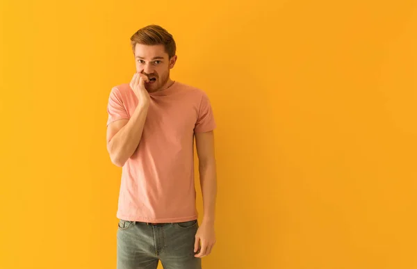 Young redhead man biting nails, nervous and very anxious