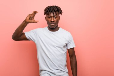 Genç Afrikalı siyahi adam işaret parmaklarıyla küçük bir şey tutuyor, gülümsüyor ve kendinden emin..