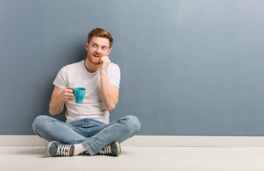 Genç kızıl saçlı öğrenci yerde oturup rahatlamış fotokopi odasına bakan bir şey düşünüyor. Elinde bir kahve fincanı var..