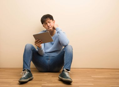 Genç Çinli adam bir fikir hakkında onun tablet düşünme kullanarak oturuyor