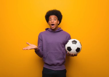 Genç Afrikalı Amerikalı sporcu elinde bir futbol topu tutarak zaferi ya da başarıyı kutluyor.