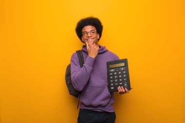 Genç Afrikalı Amerikalı bir öğrenci hesap makinesi tutuyor rahatlamış fotokopi odasına bakan bir şey düşünüyor.