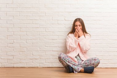 Pijama giyen genç bir kadın bir şeye gülüyor, elleriyle ağzını kapatıyor.