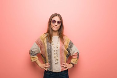 Pembe arka planda, elleri kalçasında genç bir hippi kadın.