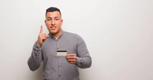 Young Latin Man Holding Credit Card Showing Number One — Stock Photo, Image