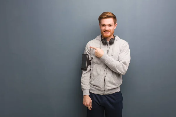 Young fitness redhead man smiling and pointing to the side