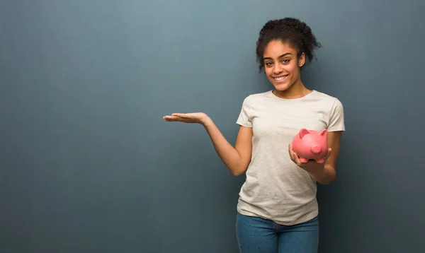 Young black woman holding something with hand. She is holding a piggy bank.