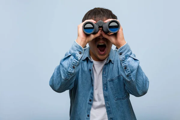 Young chinese man holding a binoculars shouting something happy to the front