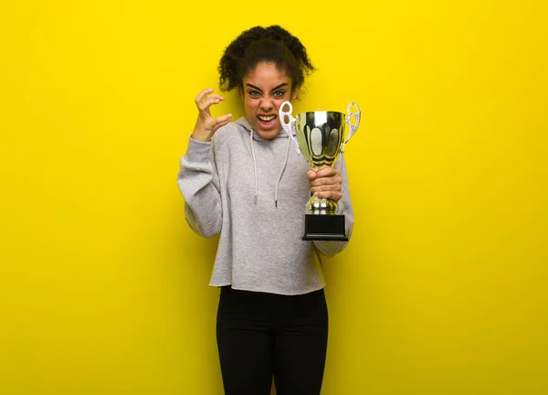 Young fitness black woman angry and upset. Holding a trophy.