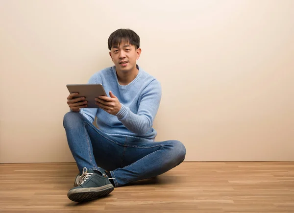 Young chinese man sitting using his tablet cheerful with a big smile