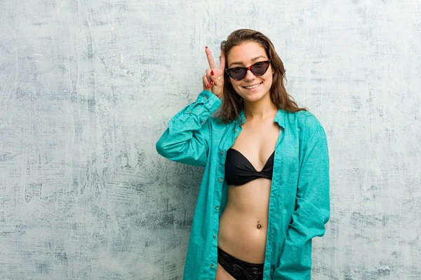 Young european woman wearing bikini showing victory sign and smiling broadly.