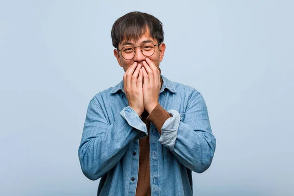 Young chinese man laughing about something, covering mouth with hands